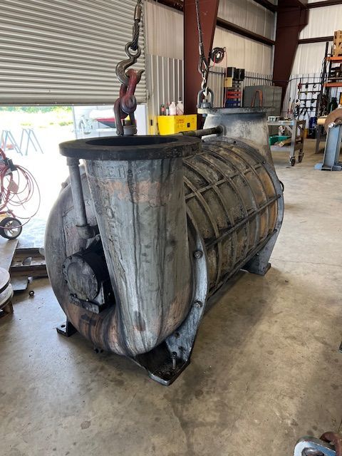 Rusty metal agricultural machinery hub with blades, shown in a workshop setting