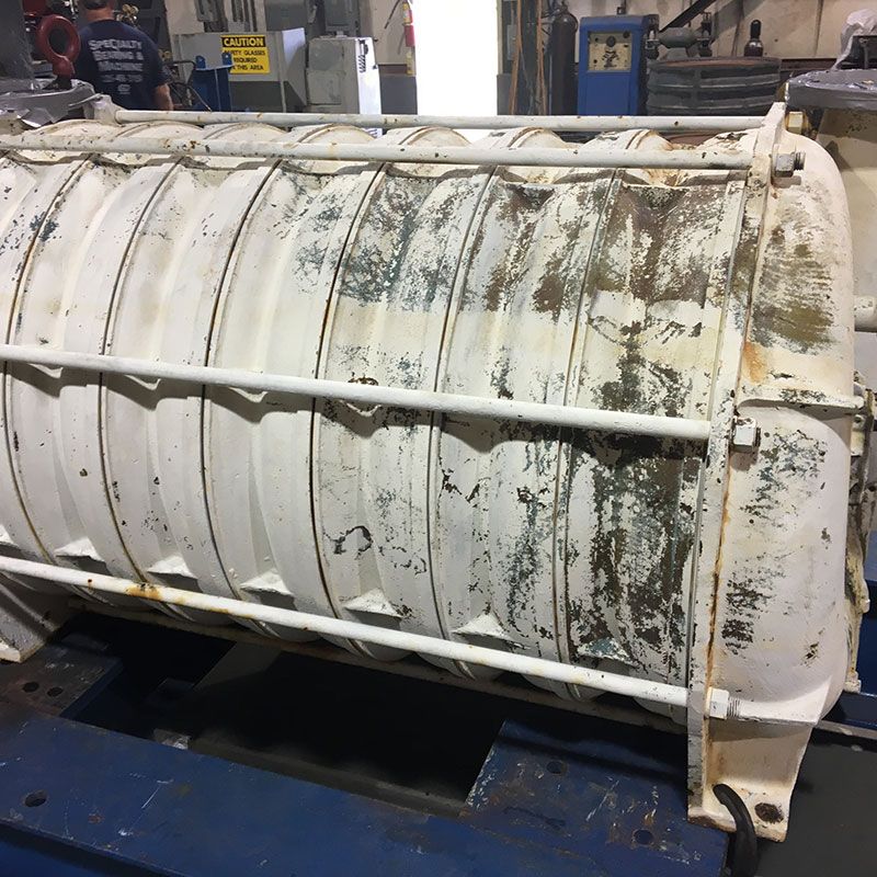Large white industrial cylindrical tank or drum with peeling paint on a blue factory floor.
