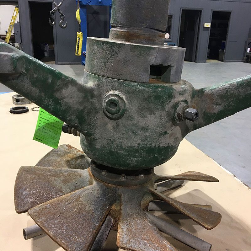 Rusty metal agricultural machinery hub with blades, shown in a workshop setting