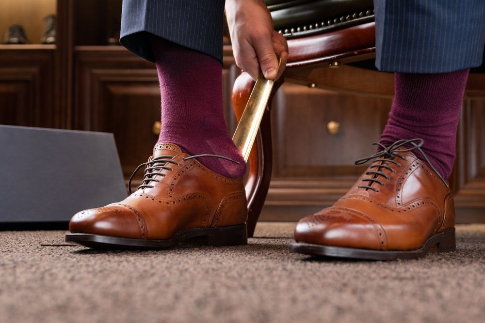A Man Wearing Purple Socks Is Polishing His Brown Shoes — New Park Suit Hire & Menswear in Airlie Beach, QLD