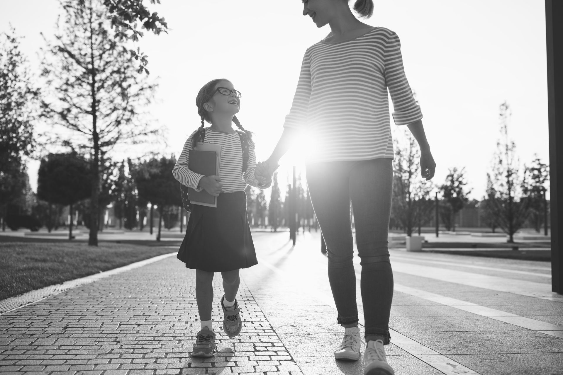 A woman and a little girl are walking down a sidewalk holding hands.