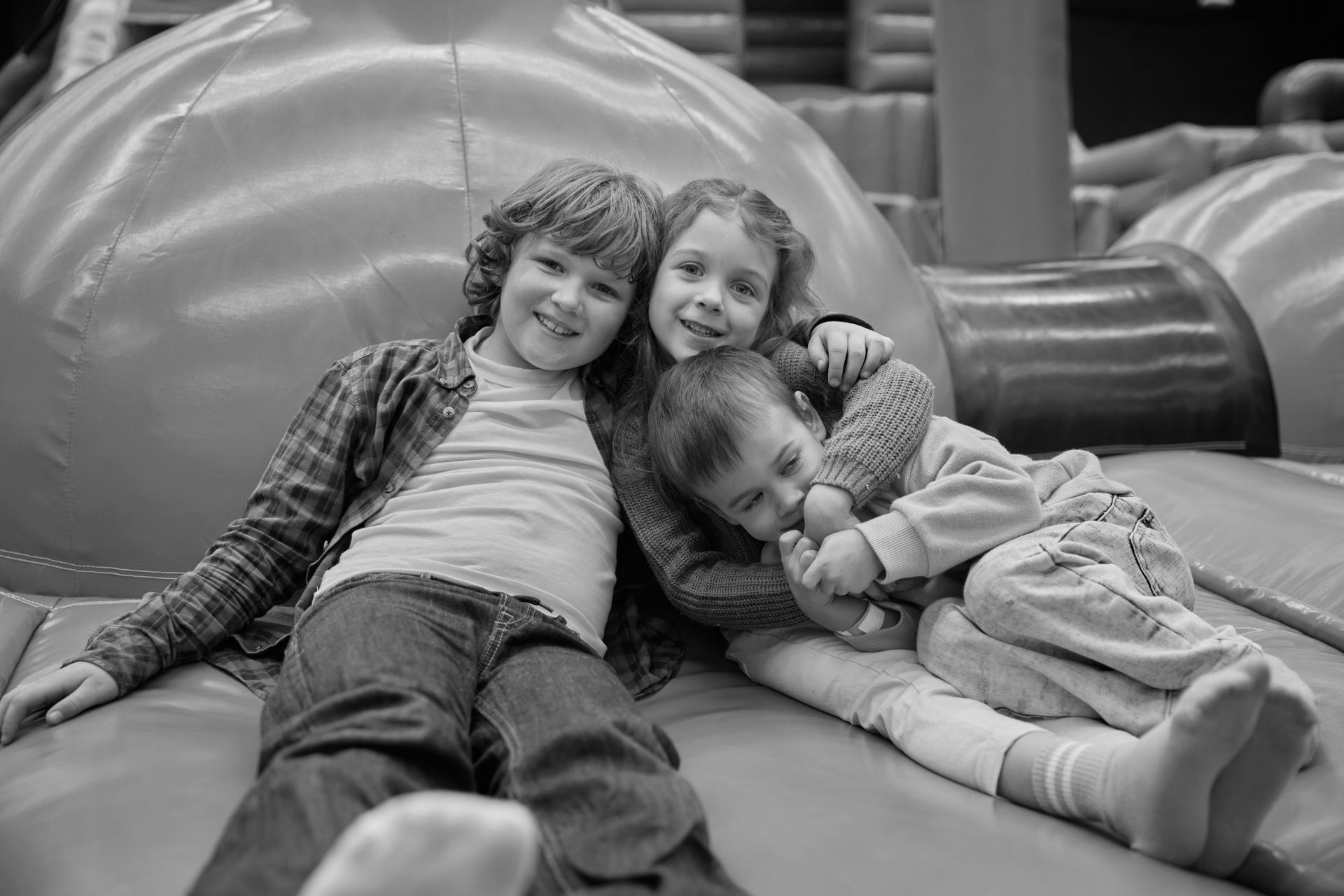 A black and white photo of three children laying on a couch.