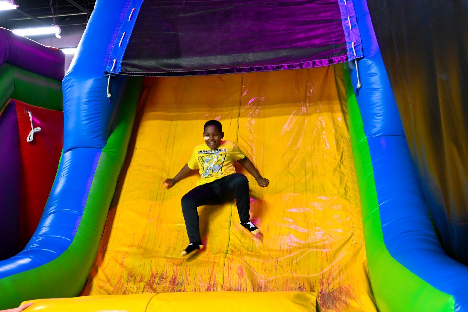 A young boy is riding down a colorful inflatable slide at Impact Fun Zone
