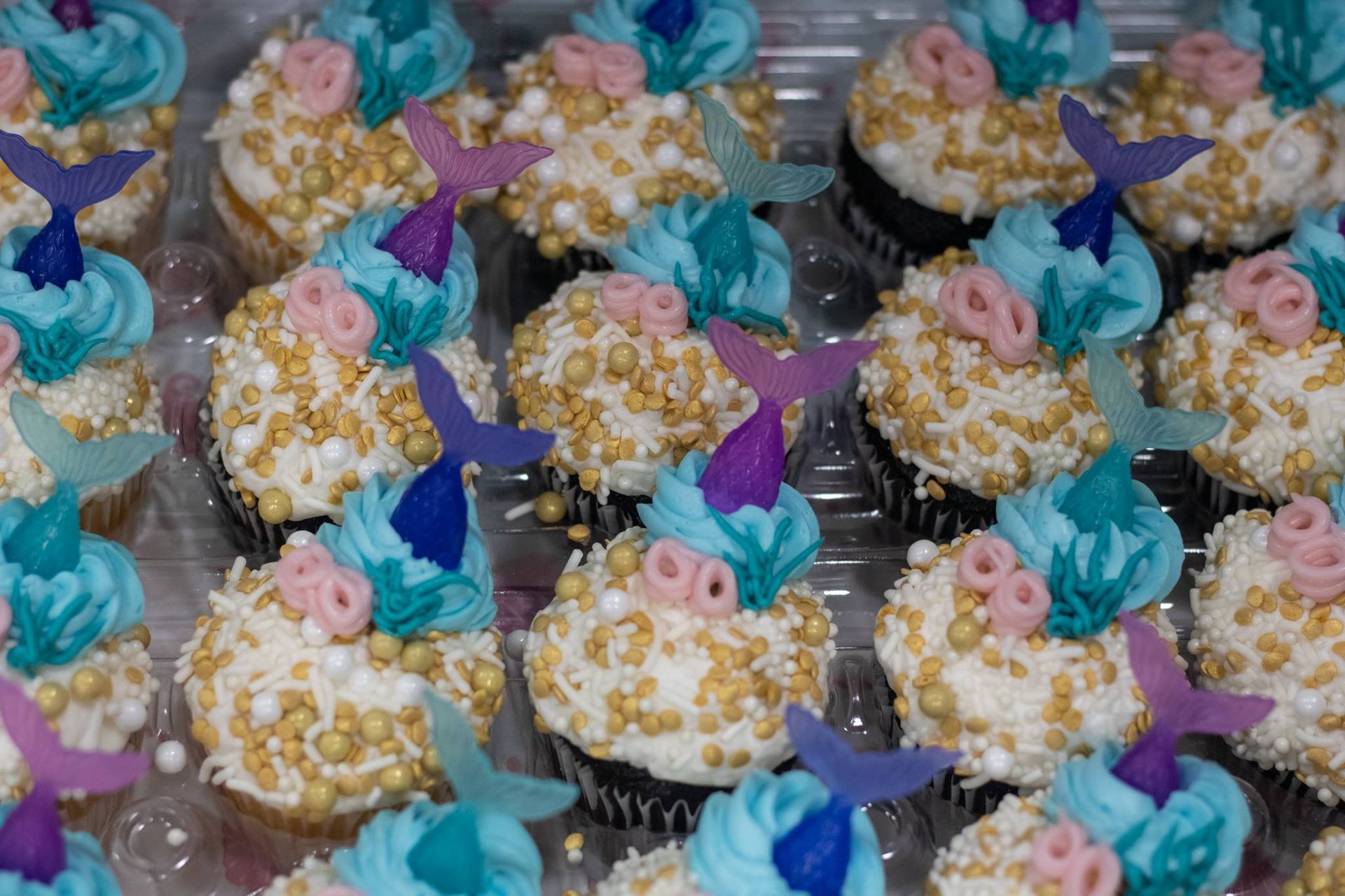 A bunch of cupcakes with mermaid tail decorations on them