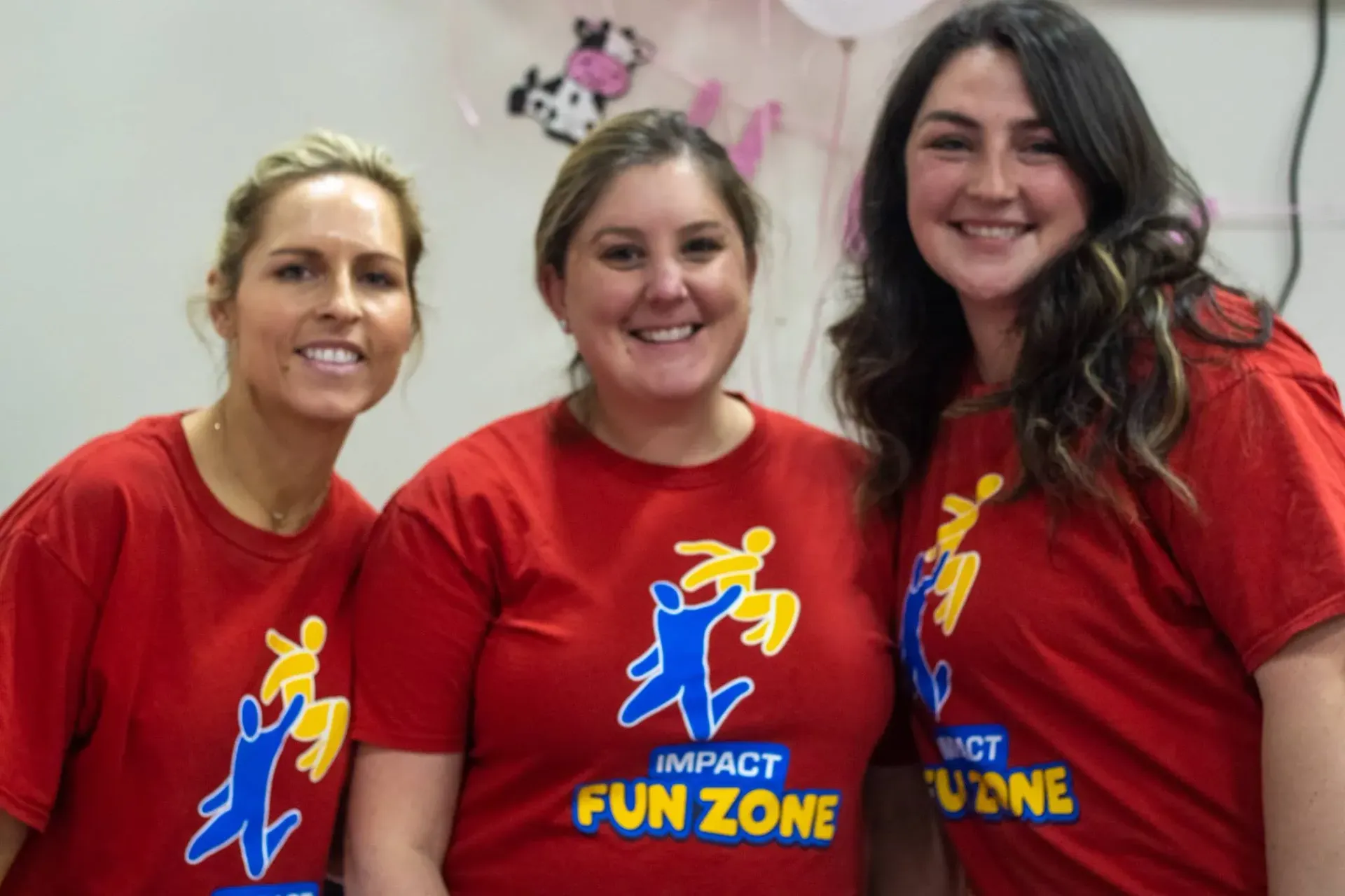 Three women wearing red shirts that say impact fun zone