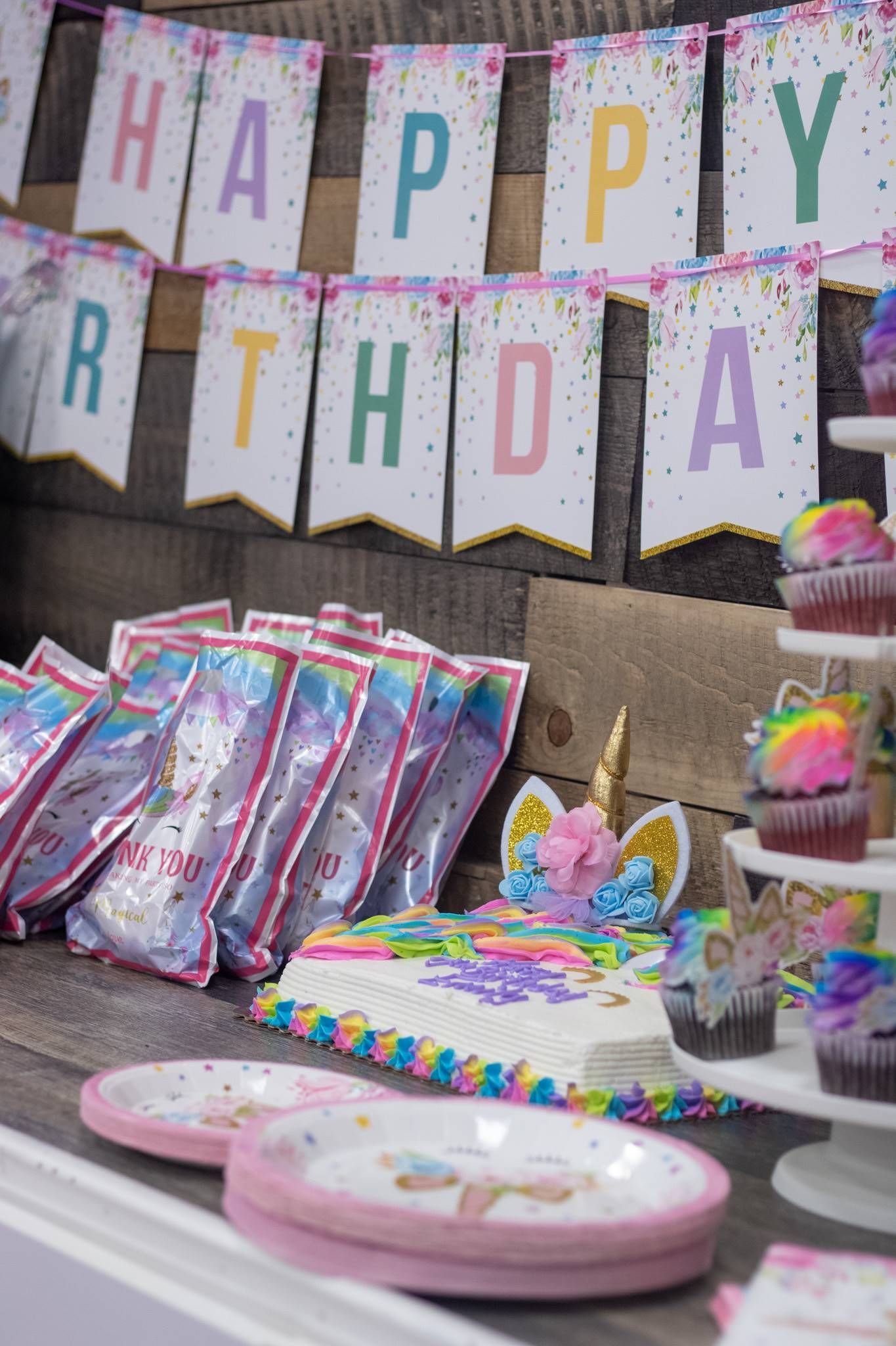 A table with a cake , cupcakes , plates , and a happy birthday banner at Impact Fun Zone