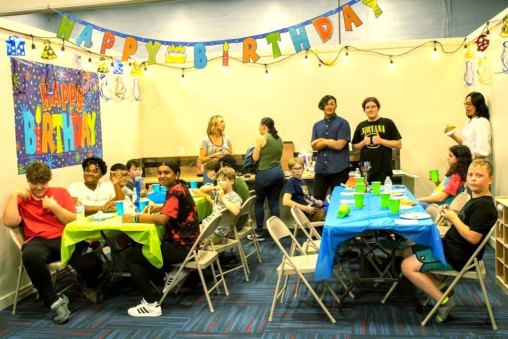 A group of people are sitting at tables at a birthday party at Impact Fun Zone