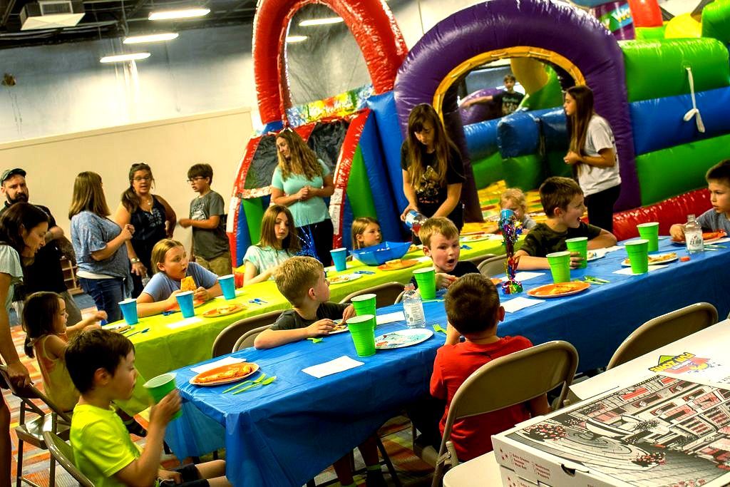 A group of children are sitting at tables at a birthday party at Impact Fun Zone