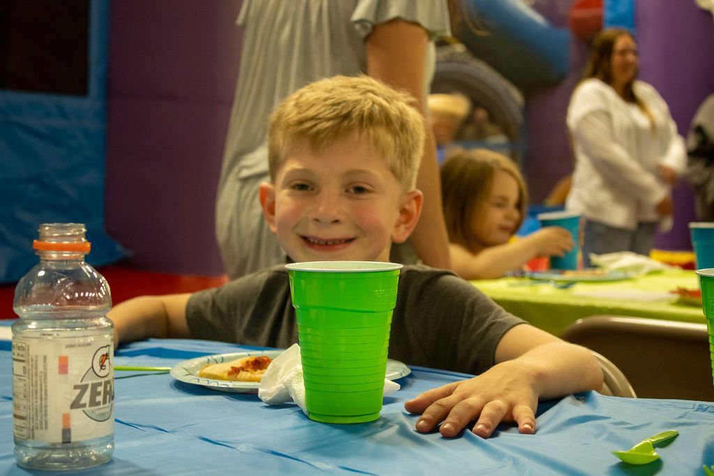 A young boy is sitting at a table with a green cup at Impact Fun Zone