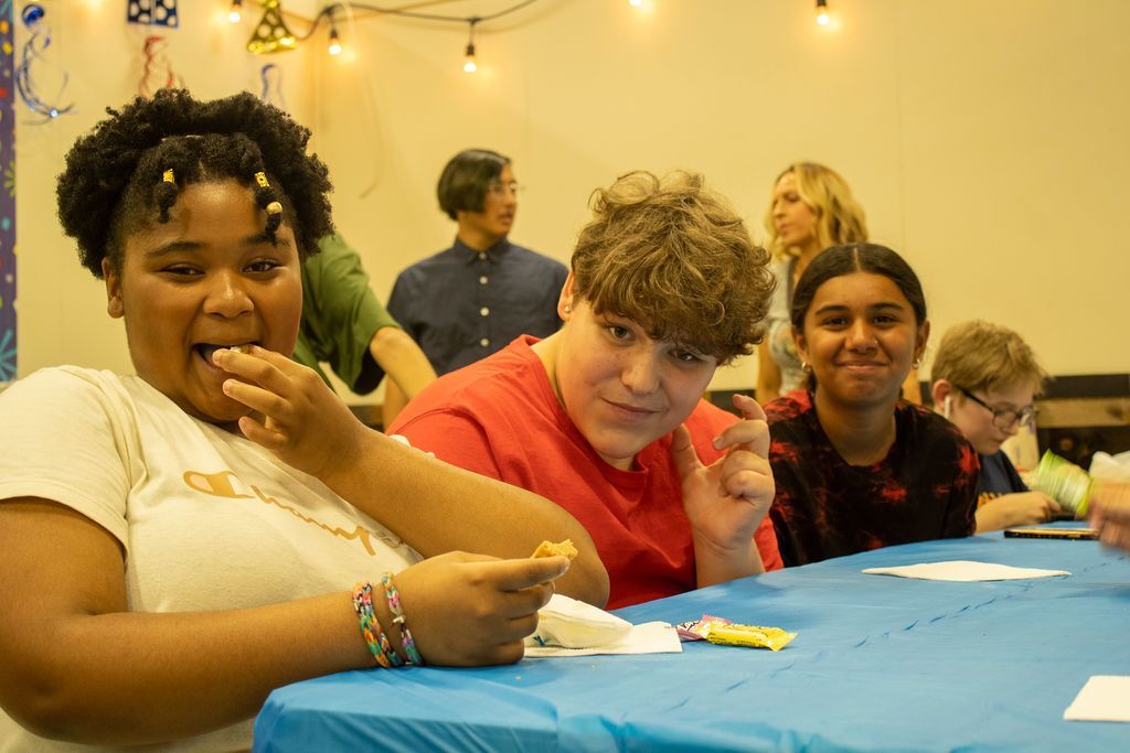 A group of young people are sitting at a table eating food  Impact Fun Zone