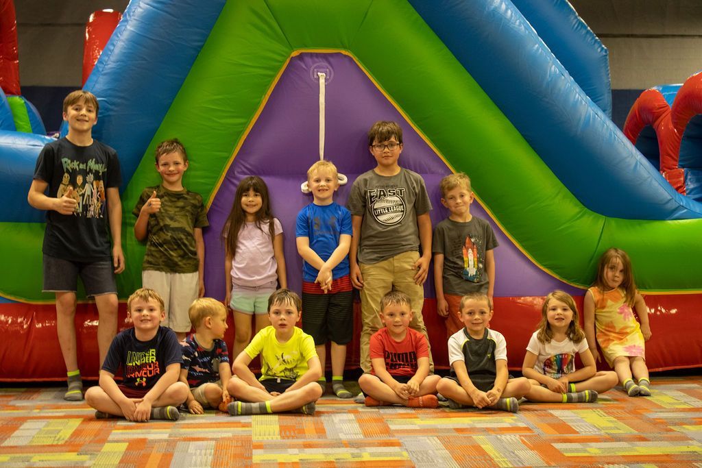 A group of children are posing for a picture in front of a bouncy house at Impact Fun Zone