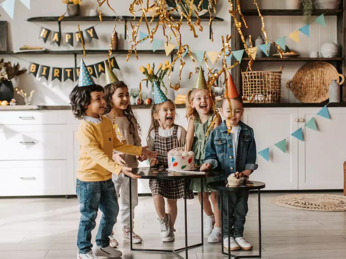 A group of children are standing around a table at a birthday party.