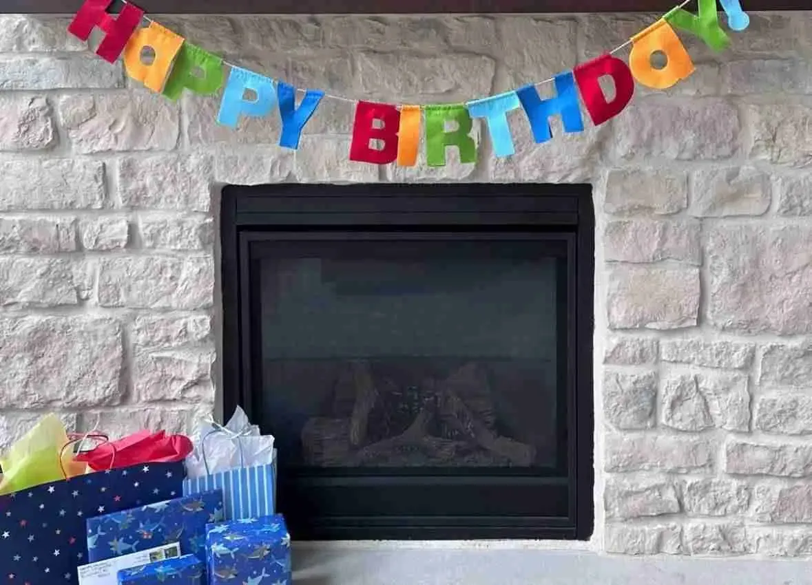 A happy birthday banner is hanging over a fireplace.