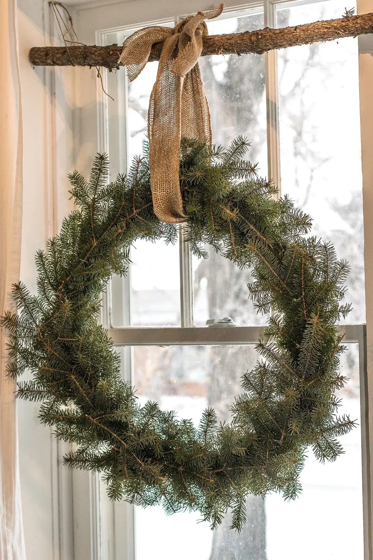 A christmas wreath is hanging on a window sill.