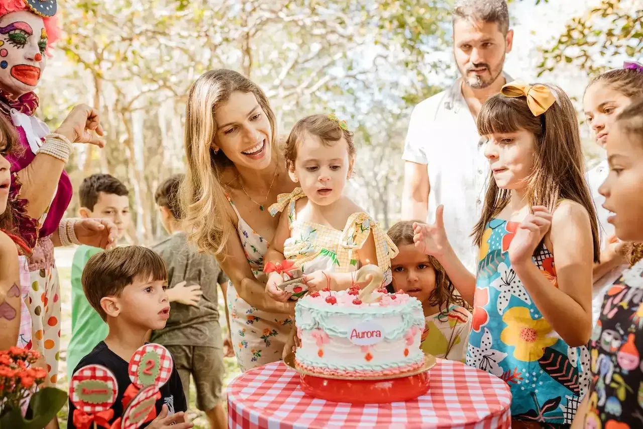 A woman is cutting a birthday cake for a little girl at a birthday party.