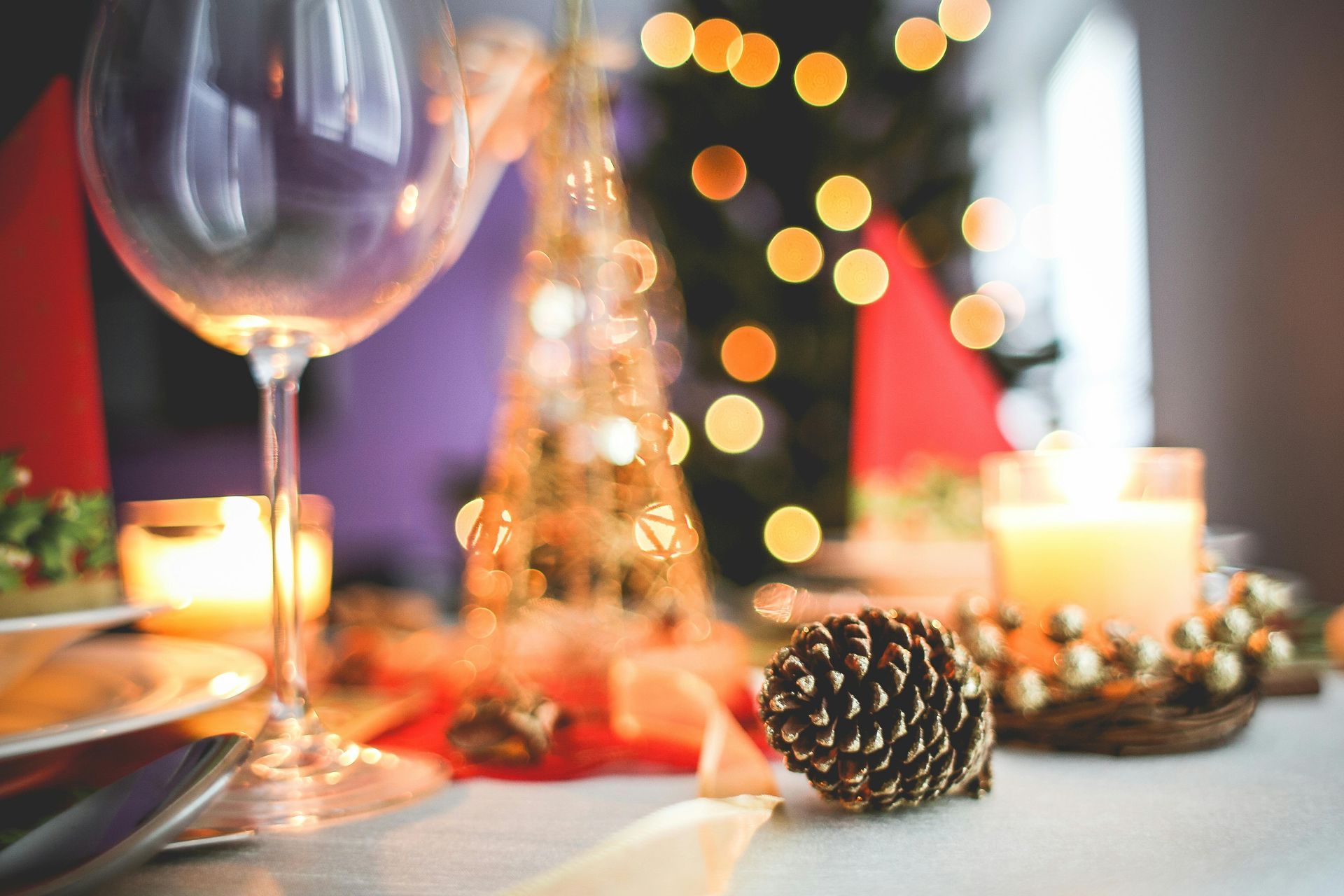 There is a christmas tree in the background and a pine cone on the table.