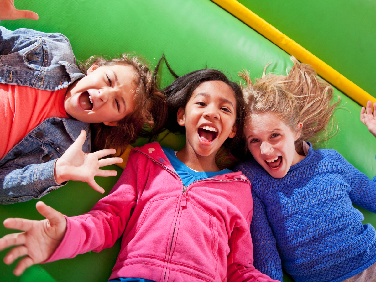 Three young girls are laying on top of a green bouncy house. Three young girls are laying on top of a green bouncy house.