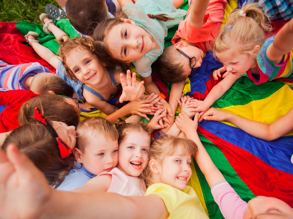A group of children are laying in a circle on a colorful parachute.