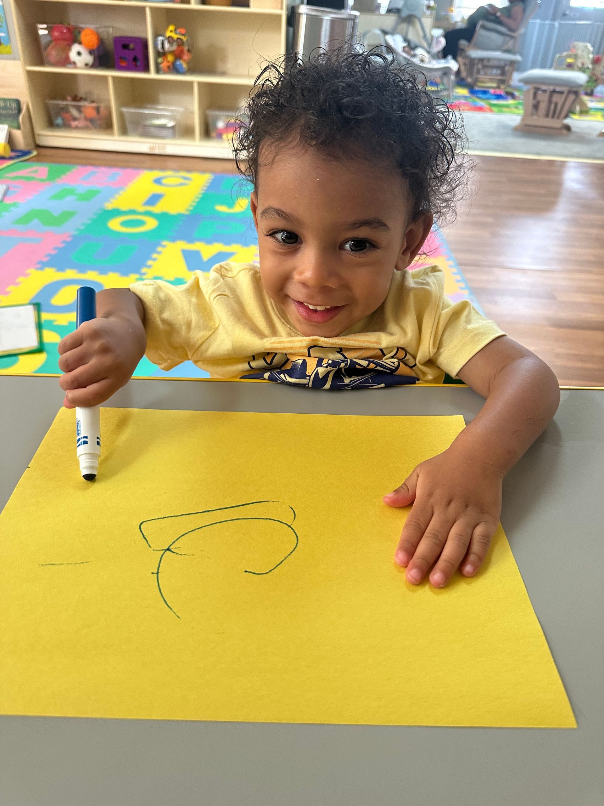 A young boy is drawing on a piece of yellow paper with a marker.