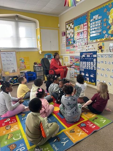 A group of children are sitting on the floor in a classroom.