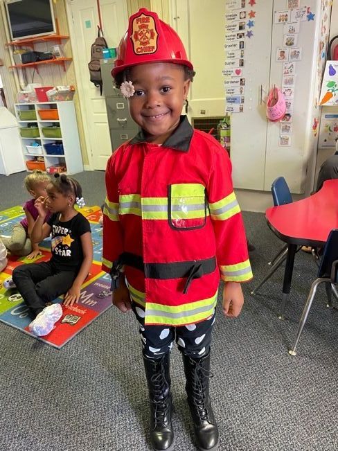 A little girl is dressed as a fireman in a classroom.