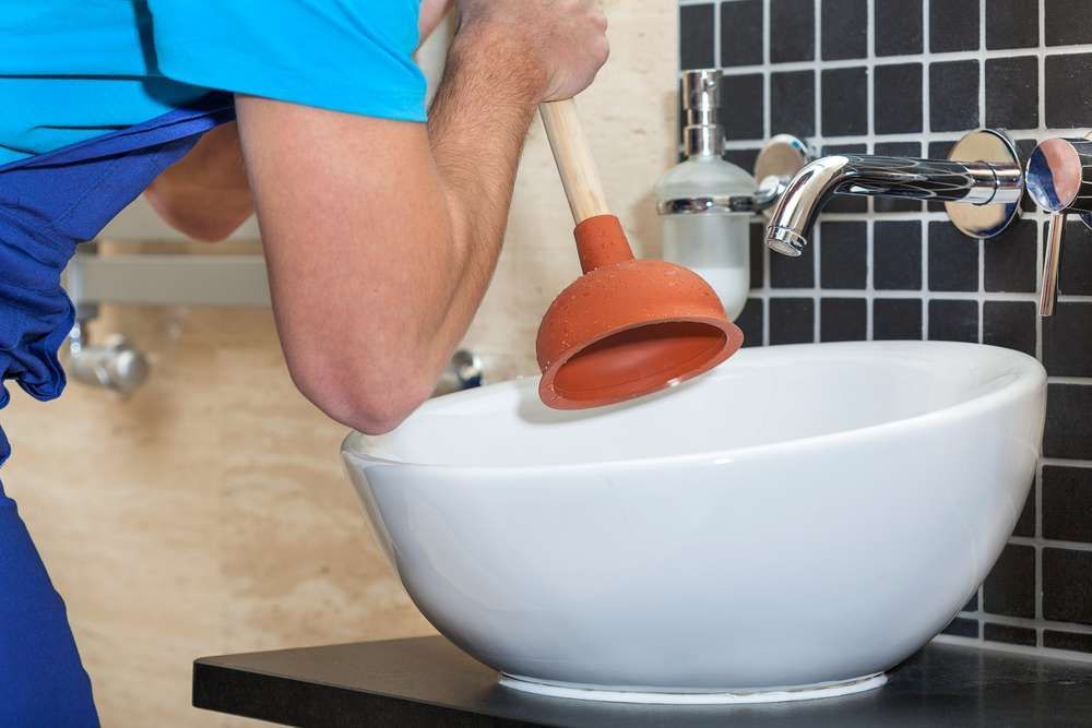 A Man Is Using A Plunger To Fix A Bathroom Sink — Hume Plumbing & Roofing Wollongong in Kiama NSW