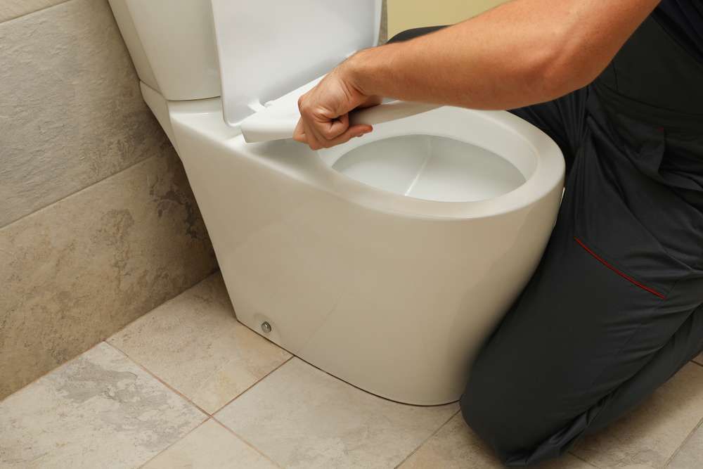 A Man Is Cleaning A Toilet In A Bathroom — Hume Plumbing & Roofing Wollongong in Woonona, NSW