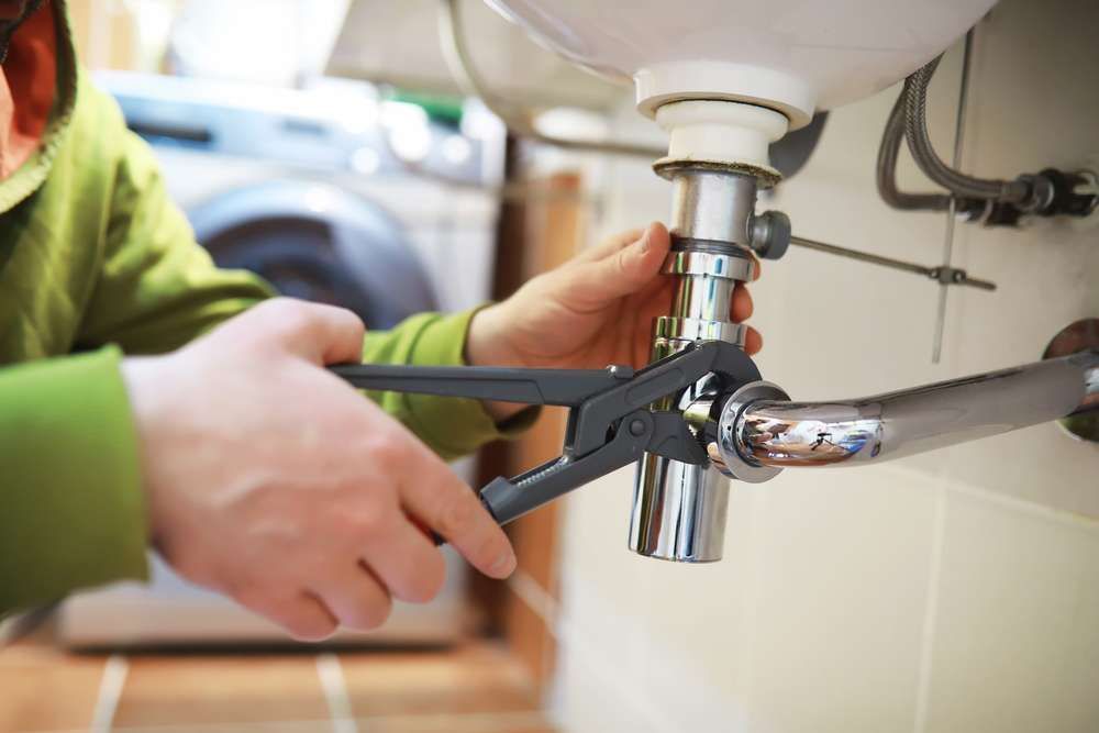A Person is Fixing a Sink With a Wrench — Hume Plumbing & Roofing Wollongong in Albion Park, NSW