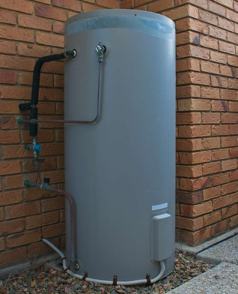 A Grey Water Heater Is Attached To A Brick Wall — Hume Plumbing & Roofing Wollongong in Shellharbour, NSW