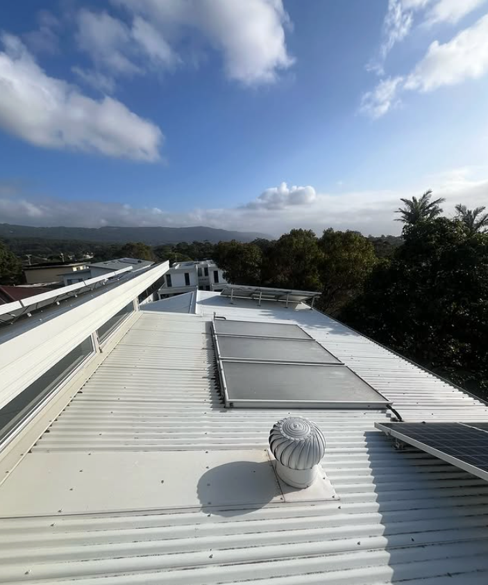 Two Construction Workers Are Working on a Metal Roof — Hume Plumbing & Roofing Wollongong in Woonona, NSW