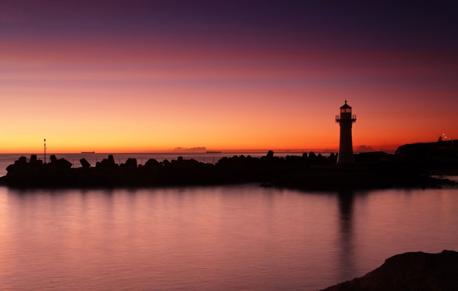 A Lighthouse is Silhouetted Against a Sunset Sky Over a Body of Water — Hume Plumbing & Roofing Wollongong in Wollongong, NSW