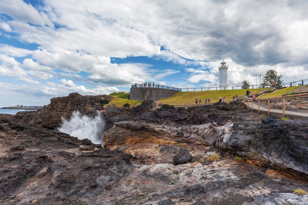 A Lighthouse is Sitting on Top of a Rocky Hill Next to a Body of Water — Hume Plumbing & Roofing Wollongong in Kiama NSW