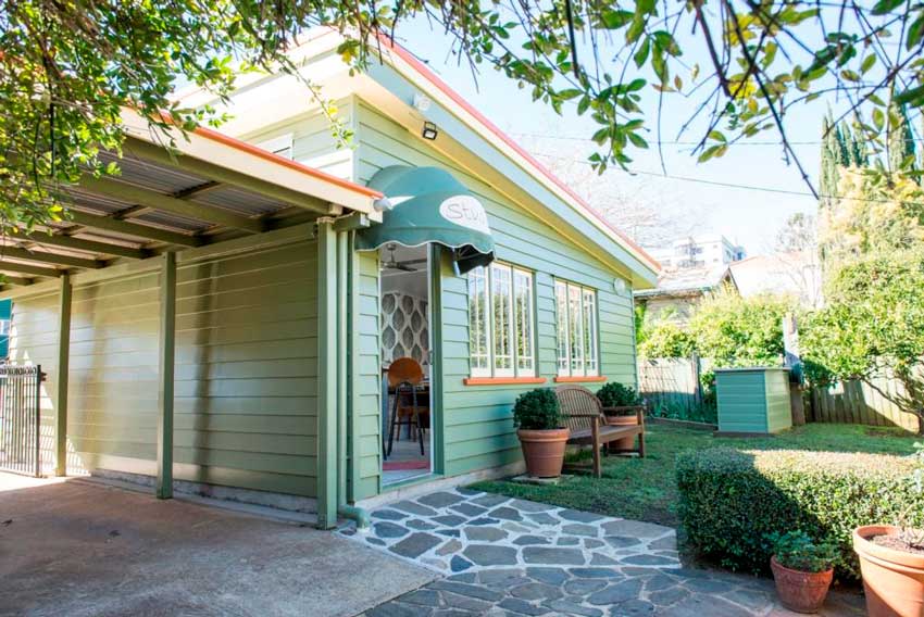 exterior of studio with green and blue siding and cobblestone floor