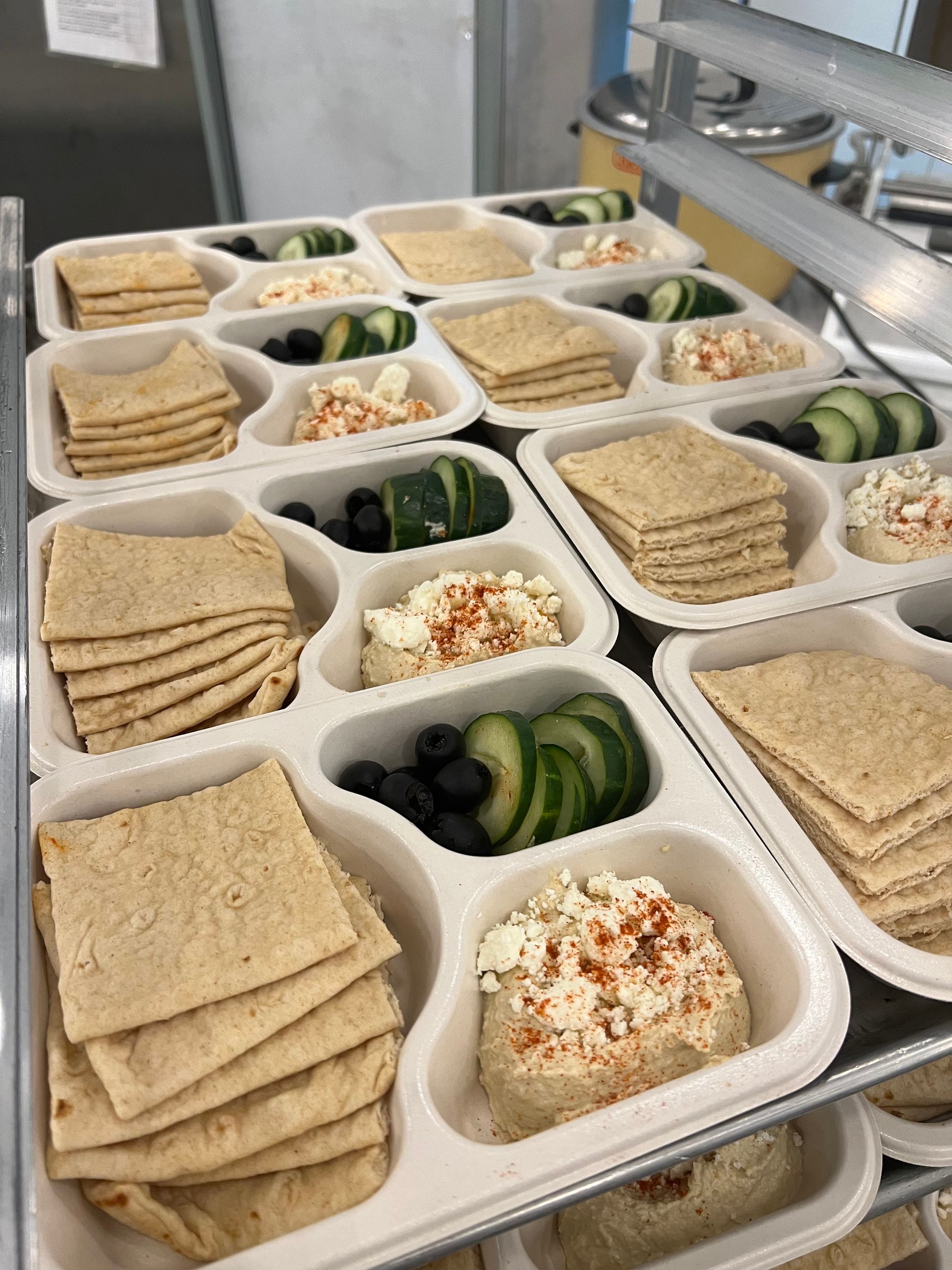 Lunch trays with hummus, crackers, cucumbers, olives, and feta.