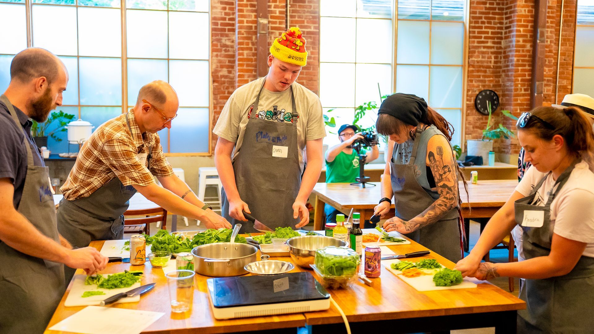 People in a cooking class, chopping vegetables at a counter in a bright kitchen.