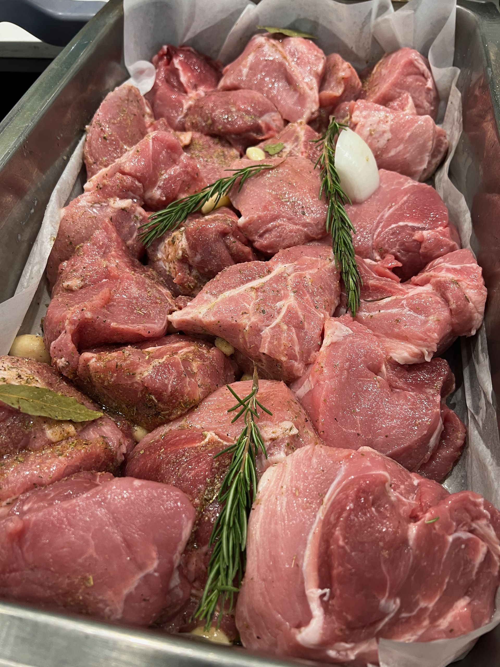 Raw pork chunks seasoned with herbs in a metal tray, ready for cooking.