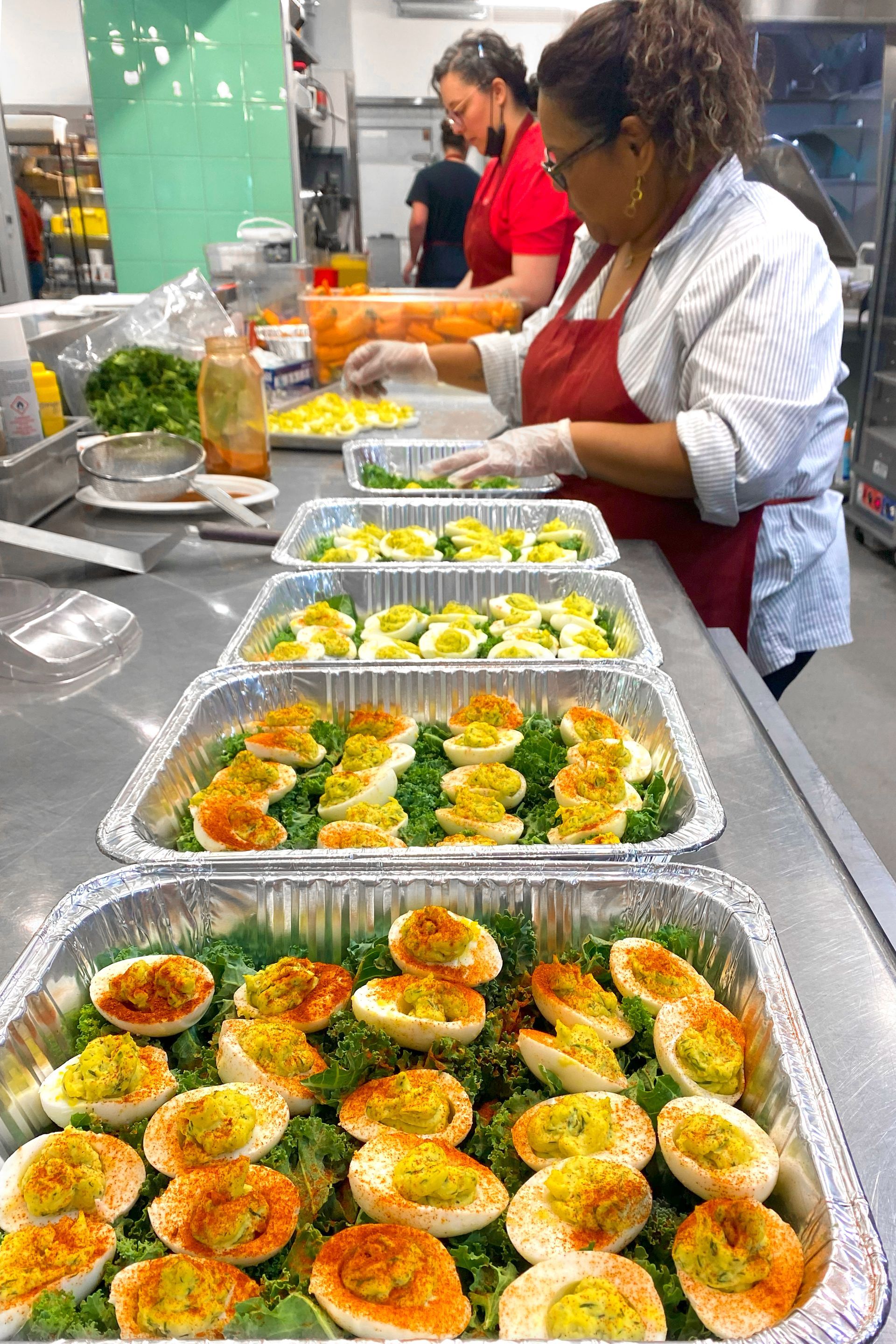 People preparing deviled eggs in a kitchen. Trays of eggs on a counter.