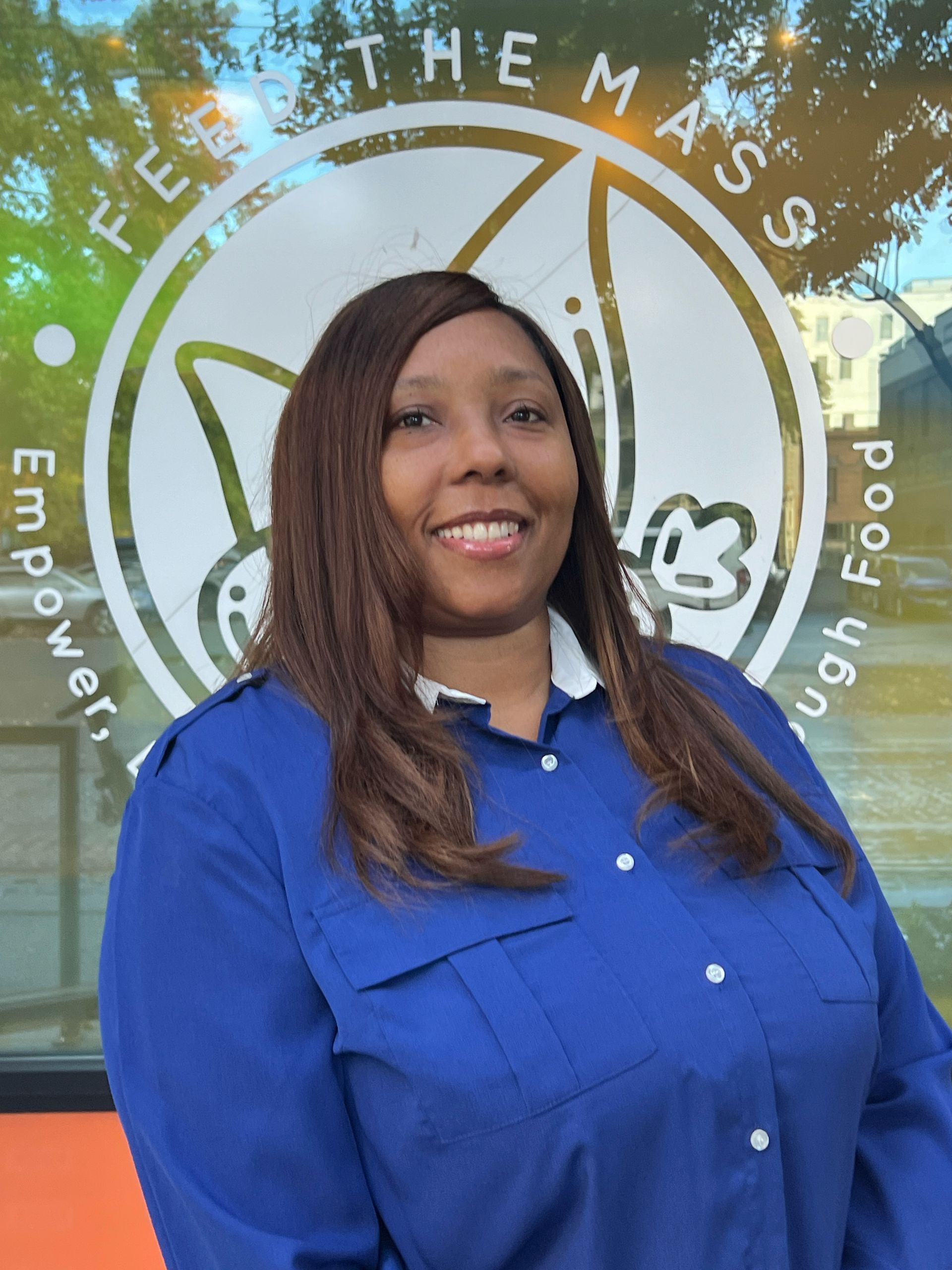 Woman in blue shirt smiles in front of a window with a logo that says