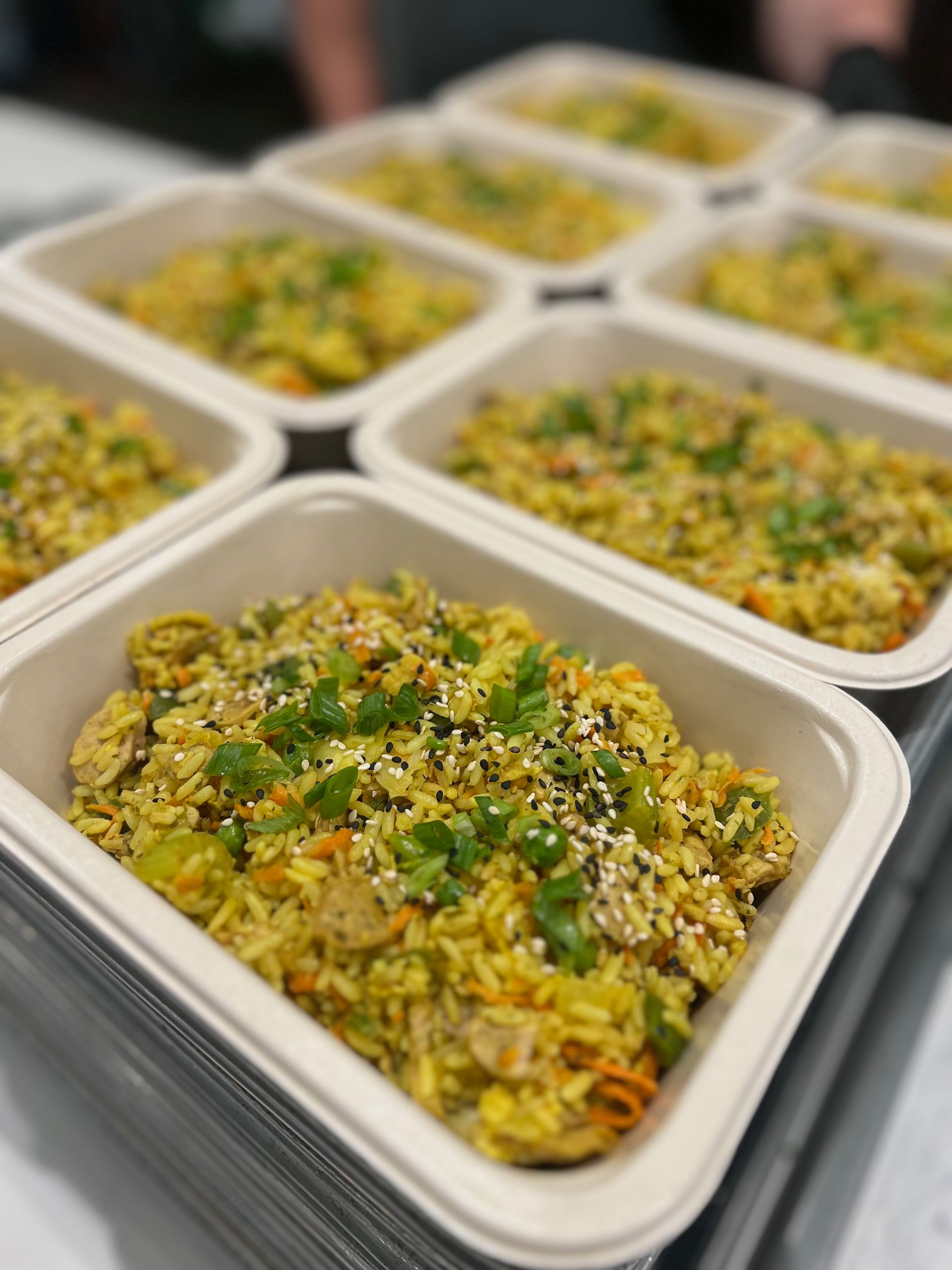 Prepared food containers filled with yellow rice, vegetables, and herbs.