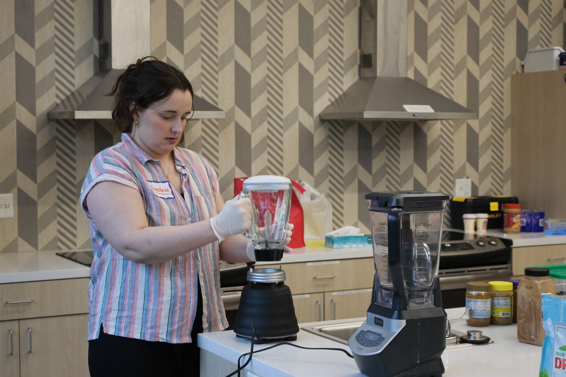 Woman in kitchen with a blender; wearing gloves, preparing food.