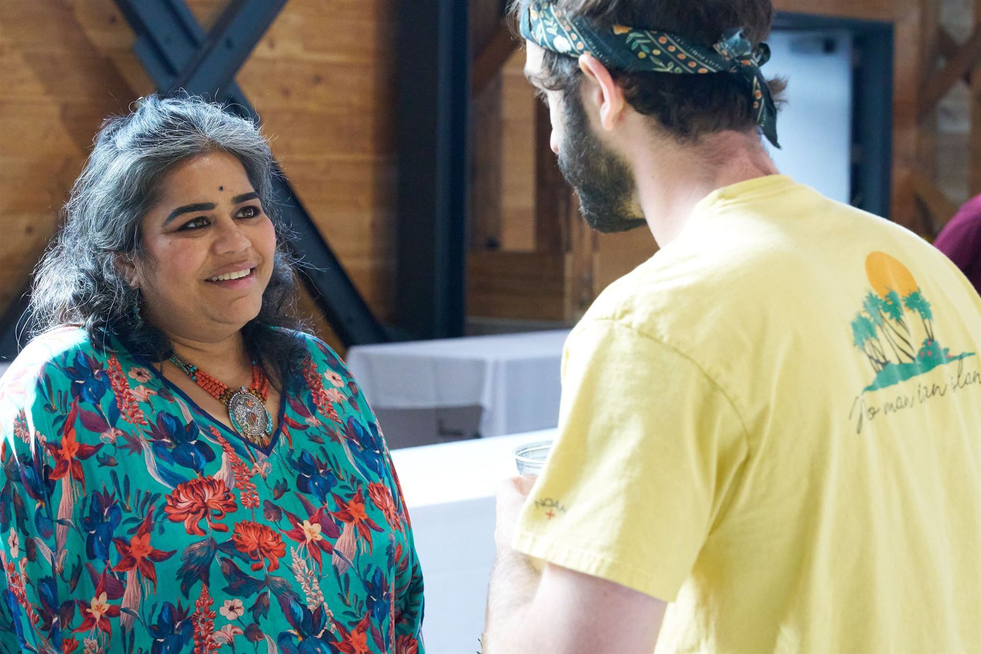 Woman in colorful floral top smiles at a man in yellow shirt, inside a building.