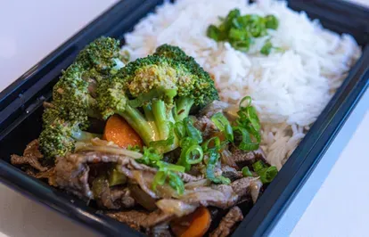 Beef and broccoli stir-fry with rice in a black takeout container, garnished with green onions.