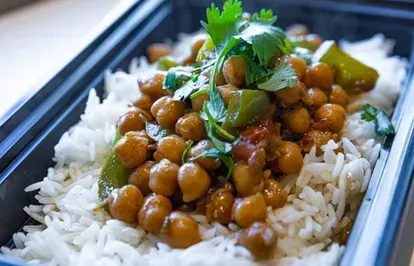 Chickpea curry over white rice, garnished with cilantro and peppers in a black container.
