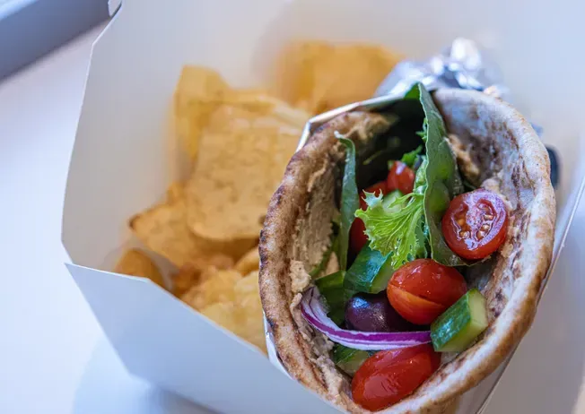 Pita sandwich filled with vegetables, next to a box of potato chips.