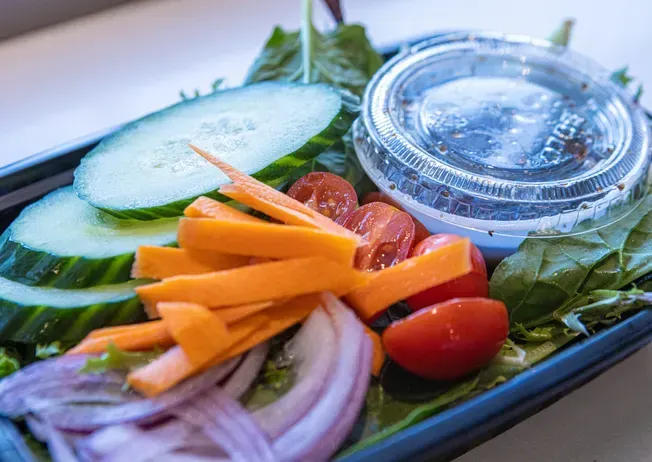 Salad with sliced cucumbers, carrots, tomatoes, red onion, and dressing container.