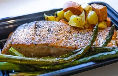 Salmon fillet with asparagus and roasted potatoes in a black container.