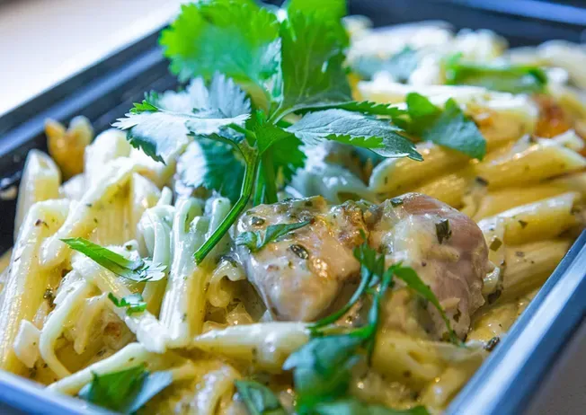 Penne pasta dish with chicken and parsley garnish in a black container.