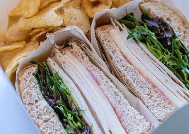 Turkey sandwich halves with lettuce and chips in a box.