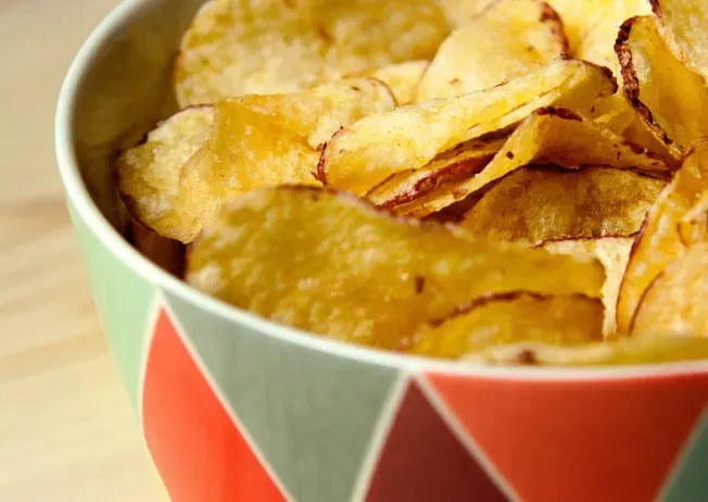 Bowl of golden potato chips with a decorative red, green and white geometric patterned bowl.