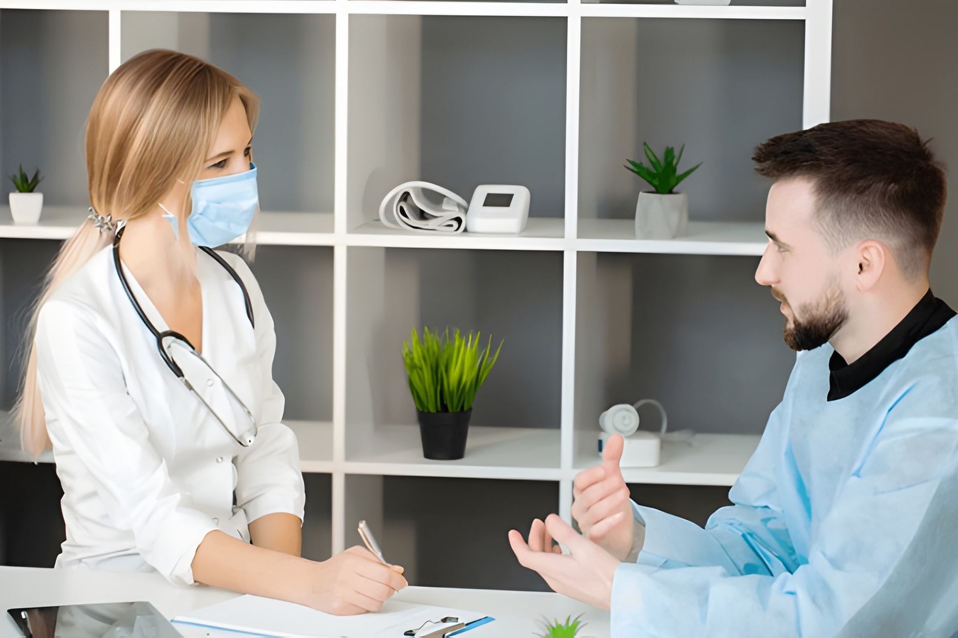 Doctor With Mask Taking Notes, Talking to Patient in Blue Scrubs — Bespoke Longevity and Aesthetic Medicine In Southport, QLD